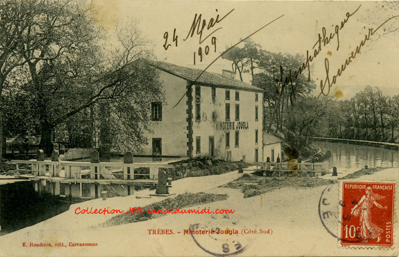 Carte postale ancienne, légendée : Trèbes  Minoterie Jougla (Côté Sud),  datée du 24 mai 1909. On aperçoit à gauche, le vantail amont de l'écluse, puis le bâtiment de la minoterie et le vantail aval de l'écluse. Ensuite, le canal du midi décrit une courbe vers la gauche pour disparaitre derrière le bâtiment.