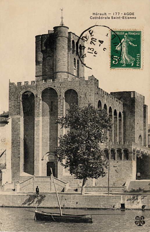 Carte postale ancienne légendée : Hérault - Agde - Cathédrale Saint-Étienne. La prise de vue est verticale On aperçoit l'Hérault 
au premier plan, une barque ancrée au milieu de l'eau, et en arierre plan, magestueuse, la Cathédrale Saint-Étienne entièrement 
construite de pierres de lave.