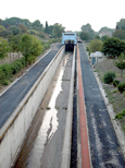 Pente d'eau de Fonsérannes vue dans son ensemble, depuis le bas de la pente. On aperçoit tout en haut le bac motorisé destiné à transporter les péniches. et au premier plan, la quasi-totalité du rail en béton sur lequel l'ensemble est destiné à rouler. Quelques filets d'eau coulent sur la piste bétonnée.