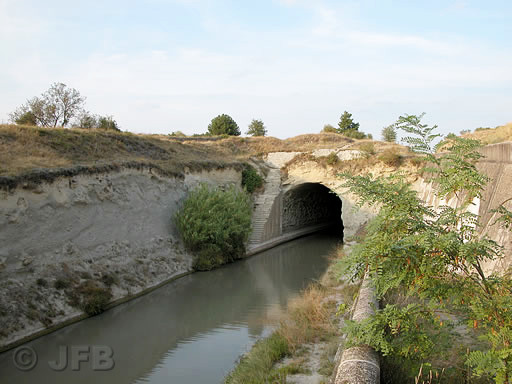 Nous sommes en été, le soleil commence a être bas, c'est la fin de l'après midi. On aperçoit le sommet aride de la Colline du Malpas, l'entrée du tunnel côté Ouest, et à gauche de l'entrée, les escaliers qui permettent de faire la liaison entre les berges du canal du midi et le sommet de la colline.