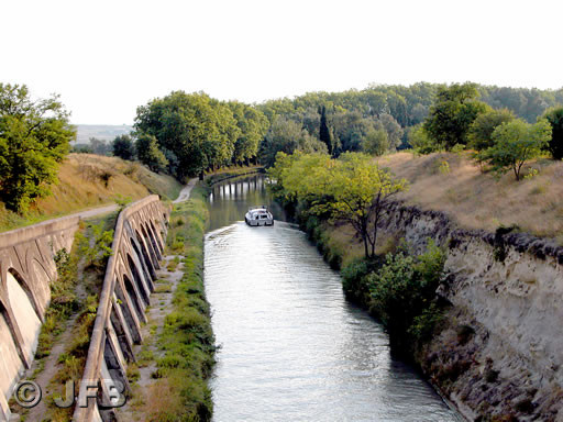 Depuis le sommet de la colline du Malpas, nous regardons vers l'Ouest. Un bateau vient de passer sous le tunnel et s'éloigne de nous. Nous sommes en été et c'est la fin de l'après-midi.