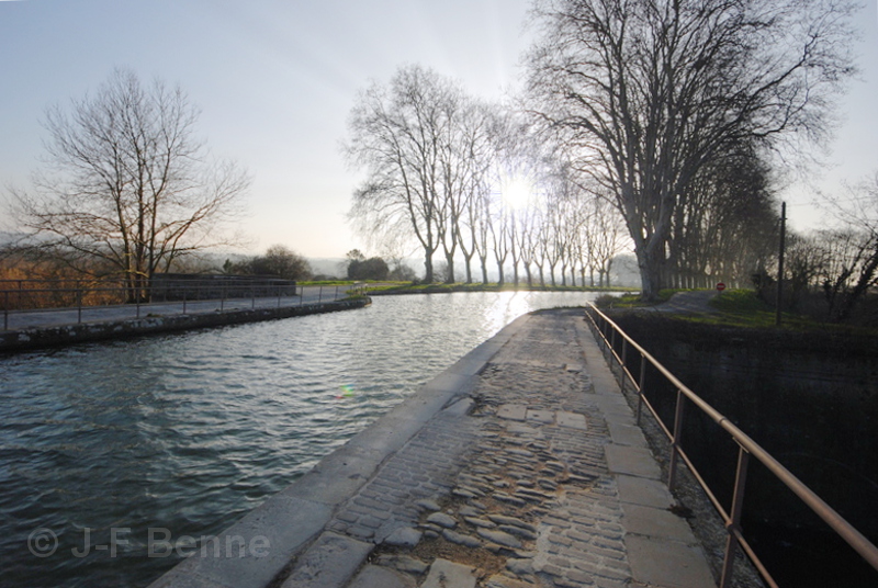 Le soleil devant, au travers des arbres encore dénudés, et le pont-canal d'Orbiel, par une fin d'après-midi