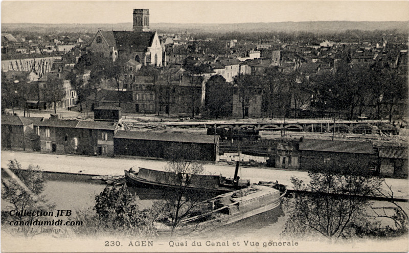 Carte postale ancienne du Canal des Deux Mers légendée : Agen - Quai du Canal et vue générale. On aperçoit très bien l'église d'Agen. Au premier plan, on peut voir une partie de la voie ferrée et le Canal. Une péniche est  amarrée, et une autre, plus grosse, est en train de maneuvrer pour accoster.