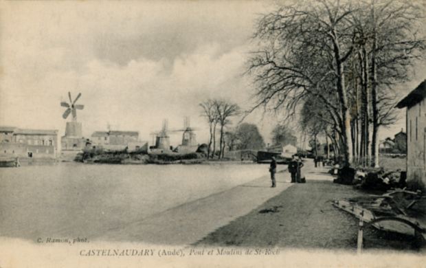Au premier plan : le Grand bassin de Castelnaudary, avec quelques promeneurs. Au loin, les trois moulins de Saint Roch