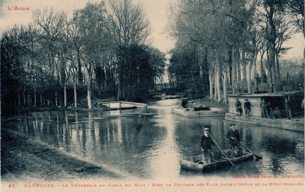 L'endroit o&ugrave; la Rigole de la Plaine se d&eacute;verse dans le Canal du Midi. Deux personnes debout sur une barque. Quatre ouvriers pr&egrave;s d'une barraque