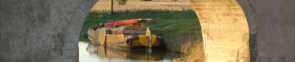 Le Canal du Midi à Argeliers par une belle fin d'après-midi. On aperçoit une belle péniche, sous un pont du canal