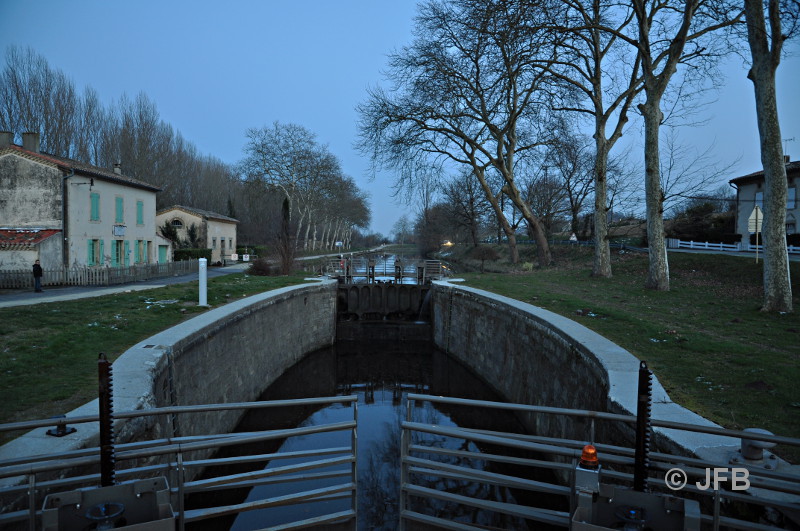 Vue d'amont de l'écluse d'Emborrel près d'Avignonet Lauragais. C'est la tombée de la nuit, on aperçoit le 
bassin de l'écluse et en perspective, le Canal du Midi. À Gauche, la maison du garde de l'écluse. La route D43 
qui va vers St-Michel-de-Lanès longe le Canal à droite sur 150 mètres environ. On aperçoit les phares d'une voiture.