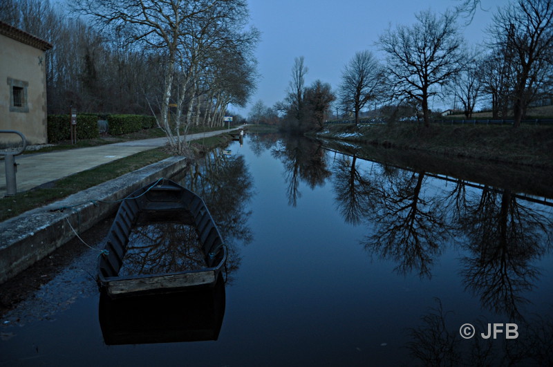 À l'écluse d'Emborrel, perspective crépusculaire sur le Canal du Canal. Les platanes dépourvus de feuilles se 
reflètent dans l'eau grâce aux dernières lueurs du jour, et au premier plan, on aperçoit une barque noyée dans 
laquelle se reflètent aussi les platanes.