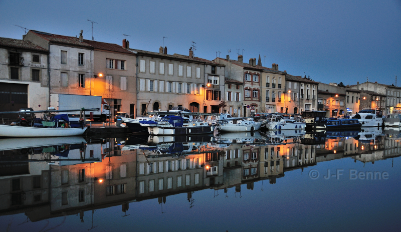 Reflets dans l'eau du port de Castelnaudary à la tombée de la nuit. De nombreux bâteaux sont 
amarrés sur le quai rive gauche, où se trouve la capitainerie. La dominante bleue sombre est compensée 
par l'éclairage public. Les eaux du canal du midi sont très calmes.