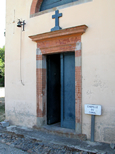 Entrée de la Chapelle de Négra : porte peinte en bleu. On aperçoit à gauche une petite cloche destinée à appeler les fidèles