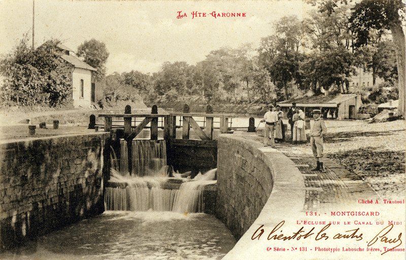 Carte postale ancienne légendée : La Haute Garonne - Montgiscard - L'écluse sur le Canal du Midi. Au premier plan, la porte amont de l'écluse près de laquelle se trouve une famille de promeneurs. Plus loin, derrière ce groupe, on voit le lavoir dans lequel se trouvent quelques lavandières.