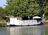 Une belle petite péniche toute blanche. Seule, une petite partie au dessus de la ligne de flotaison est noire... Cette péniche est vraiment faite pour l'habitation. L'arrière, bien plus haut que la partie habitable, doit servir de cabine de navigation. Le timon doit se trouver à l'intérieur. Cinq fenêtres sur la partie habitable, sont ornées de rideaux, qui interdit la vue à l'intérieur, c'est très mignon ! De surcroit, sur l'avant, espace dégagé, un grand parasol blanc, parfaitement assorti à la péniche. C'est sublime !