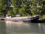 Une belle péniche simple, comme autrefois, mais repeinte de frais, apparemment non aménagée pour l'habitation. La coque est de couleur noire et unebande blanche horizontale l'agrémente. Le pont est également de couleur blanche. Elle est magnifique !