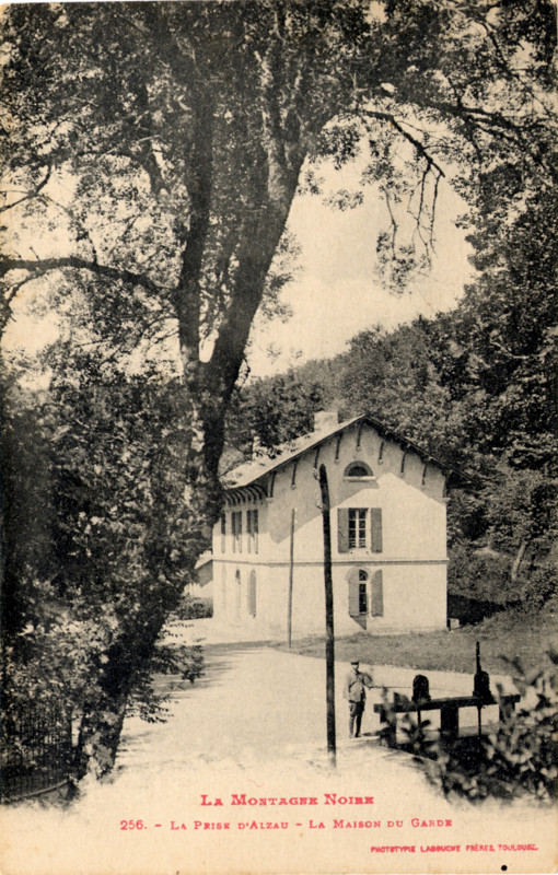 Carte postale ancienne légendée : La Montagne Noire - La prise d'Alzau - La maison du garde.
	Il s'agit d'une photo verticale. On aperçoit au tout premier plan un arbre qui se penche vers la maison
	du garde. Un peu plus loin, un homme se tient près de la prise d'eau. Un peu plus loin, on voit la maison
	du garde...