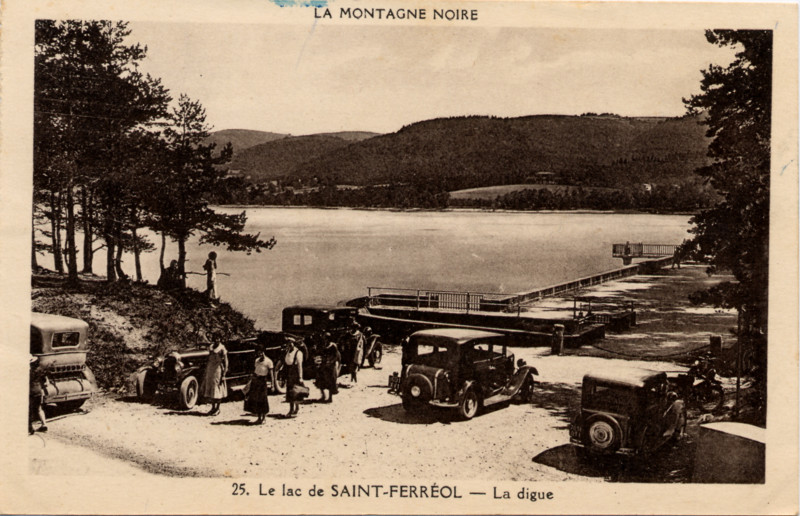 Un dimanche au lac de Saint-Ferréol. Le lac est presque plein, on aperçoit la digue et les constructions permettant de déverser le trop plein. Quelques promeneurs et quelques anciennes automobiles.