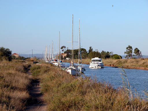 Lumière rasante sur le sentier qui longe le canal près de l'embouchure. Un bateau vogue vers nous, quelques autres sont amarrés