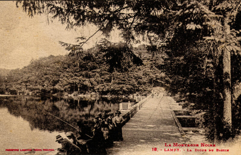 Perspective de la digue du bassin de Lampy, avec à gauche, le lac. Quelques pêcheurs et quelques promeneuses et promeneurs se trouvent sur cette digue.