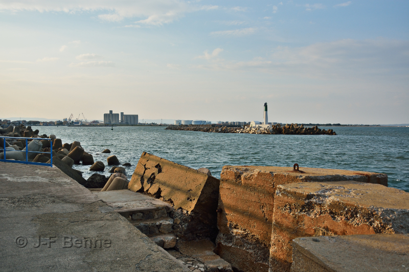 Vue de Port La Nouvelle, mais surtout des installations portuaires, depuis la jetée menant au phare rouge. Nous apercevons donc le phare vert (blanc, dont le sommet est vert), un peu plus loin, toujours sur l'autre rive, les installations portuaires et le chenal qui nous mêne à la mer