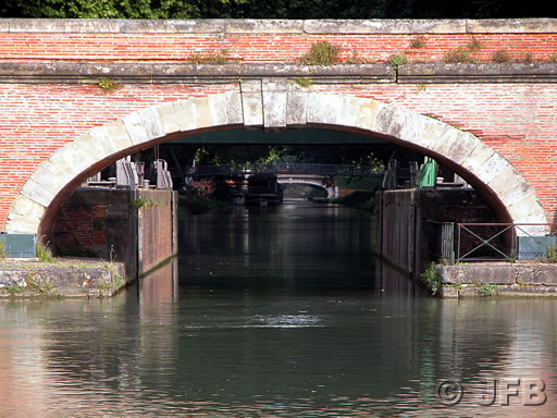 Prise de vue au télé-objectif, sous l'un des ponts jumeaux dont le parapet est éclairé par le soleil, le Canal de Brienne continue dans l'ombre...