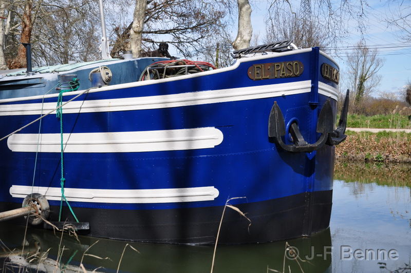 Proue d'une péniche d'habitation peinte en bleu foncé avec dee belles lignes blanches. Deux grosses ancres sont peintes en noir. Son nom : El Paso, est gravé sur une grosse plaque en bronze.