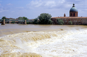 La crue est telle que la différence de niveau entre le haut et le bas de la chaussée est réduite de moitié. La Garonne se comporte comme un torrent boueux, et l'eau forme de violents remous. Sur l'autre rive, on aperçoit le dôme de la Grave